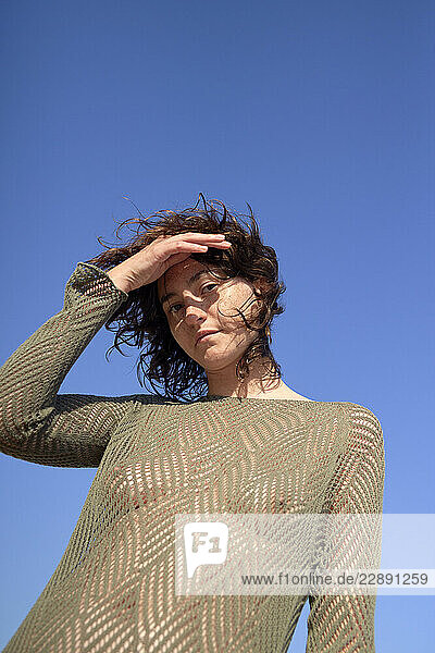 Woman in green mesh top posing under a clear blue sky while shielding her eyes.