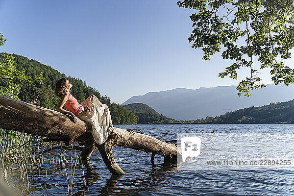 Woman lying on fallen tree at lake