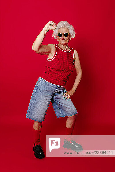 Senior woman in stylish outfit posing energetically against a red background