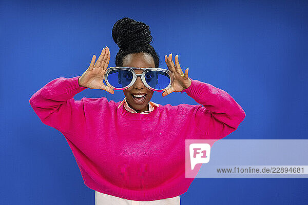 Young female entrepreneur with mouth open wearing novelty glasses against blue wall in office