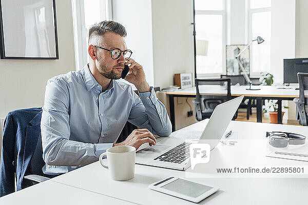 Male entrepreneur talking on mobile phone while using laptop at office