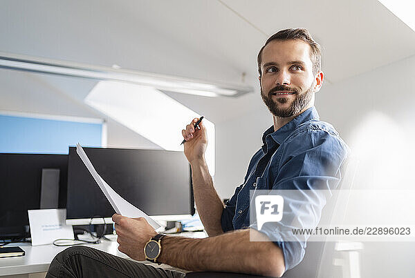 Young entrepreneur with paper looking away while sitting at office