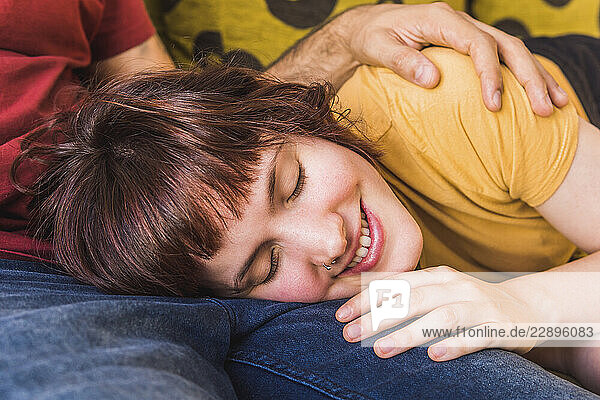 Smiling beautiful woman resting on boyfriend s lap at home