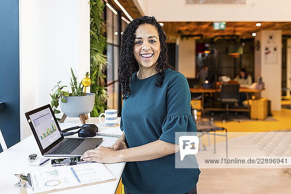 Smiling businesswoman with laptop on desk at office