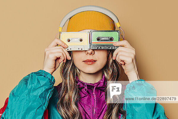 Woman in 80s tracksuit hiding face with cassettes and wearing headphones