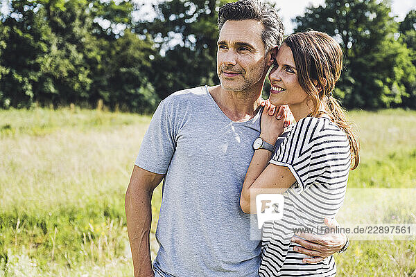 Man with arm around on smiling woman standing at meadow