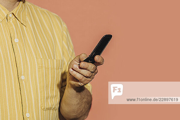 Mid adult man in yellow shirt holding a flip phone against an orange background