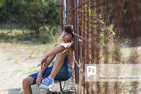 Boy sunbathing while leaning on a rusty fence