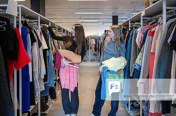 Two young women browsing clothes at second hand clothing store