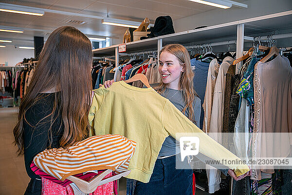 Two young women browsing clothes at second hand clothing store