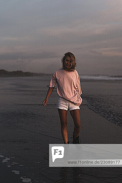 Woman walking along beach at sunset in pink shirt and white shorts