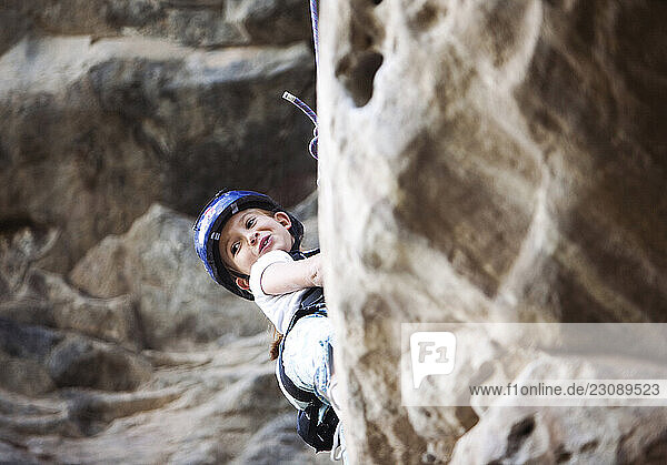 A young girl wearing a rock climbing helmet looks out from the rock as she sets out to climb a sport route at Santa Clara in Ecuador.